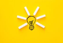 A creative idea concept with wooden blocks forming light rays around a drawn lightbulb on a bright yellow background