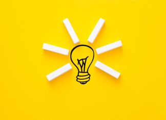 A creative idea concept with wooden blocks forming light rays around a drawn lightbulb on a bright yellow background