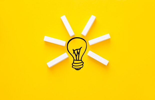 A creative idea concept with wooden blocks forming light rays around a drawn lightbulb on a bright yellow background