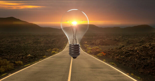 A clear light bulb framing a sunset over a road in a volcanic landscape symbolizing innovation