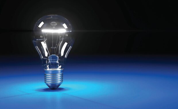 A clear lightbulb representing innovation on a blue surface with a dark background