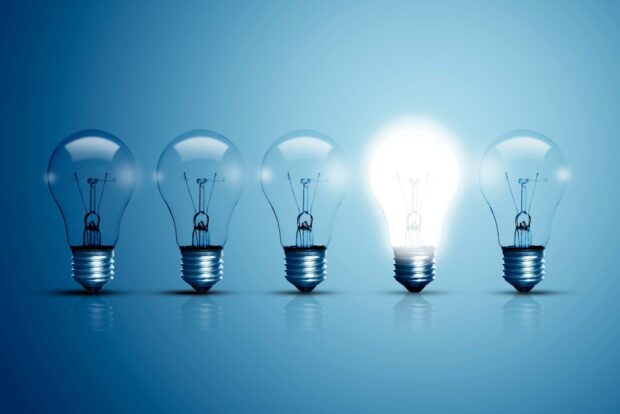A glowing light bulb representing innovation among unlit bulbs on a reflective surface