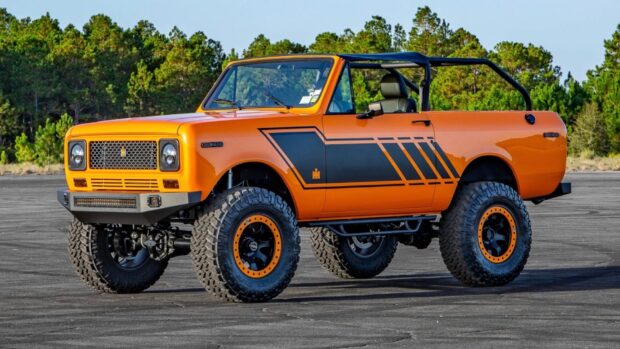Orange International Harvester truck with off road tires parked on asphalt with trees in background