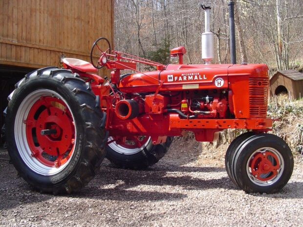 Vintage International Harvester Farmall tractor in red color parked near wooden barn