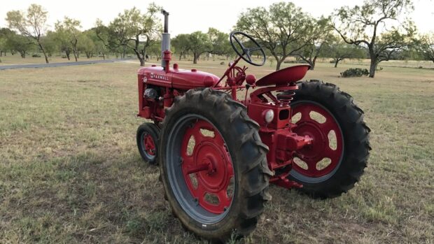 A red International Harvester tractor is parked on grassy land with trees in the background