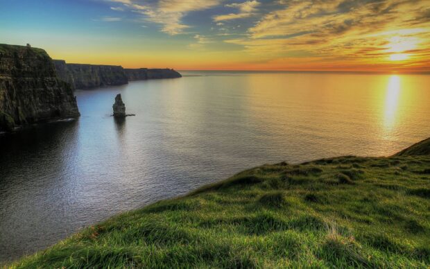 Cliffs and grassy fields in the Irish countryside at sunset with calm ocean waters and clear skies