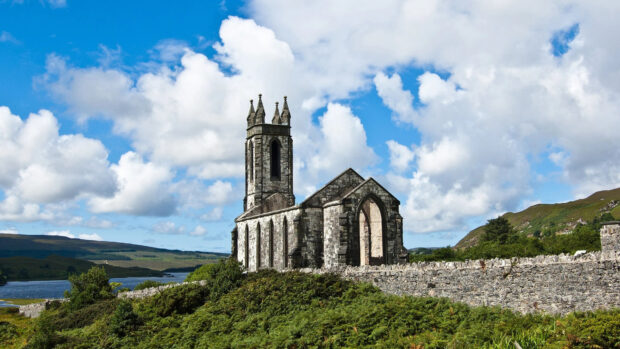 Ruins of an ancient stone church in the Irish countryside under a blue sky with clouds