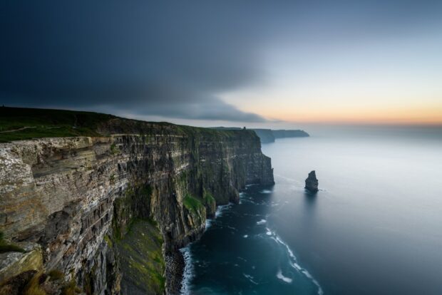 Dramatic Irish countryside cliffs overlooking the calm sea at sunset with green grass on top