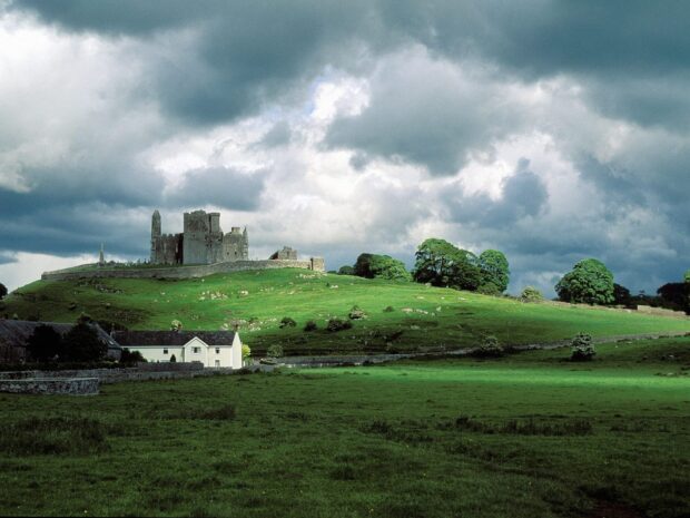 Historic castle ruins on green fields in Irish countryside scenery with cloudy sky