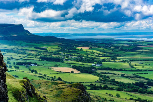 Rolling green hills and farmland in the Irish countryside under a cloudy blue sky