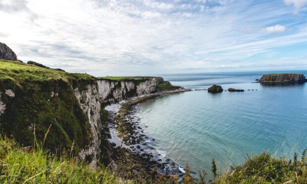 Rugged cliffs and rocky shoreline of the Irish countryside with calm blue waters under a cloudy sky