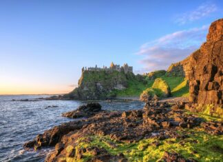 Ancient castle ruins on the Irish countryside coast with rocky cliffs and lush greenery at sunset