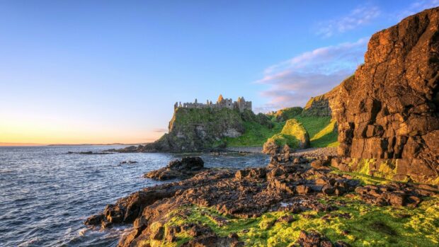Ancient castle ruins on the Irish countryside coast with rocky cliffs and lush greenery at sunset
