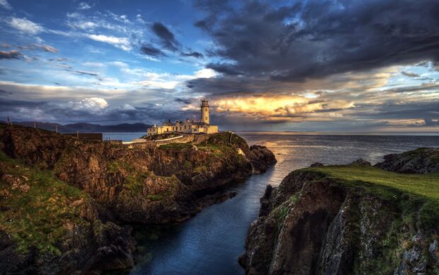 A lighthouse stands on rugged cliffs in the Irish countryside under a dramatic sky