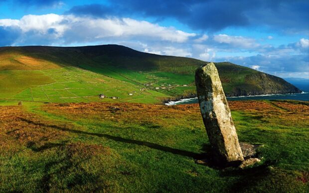 Ancient standing stone in the Irish countryside with green hills and ocean in the background