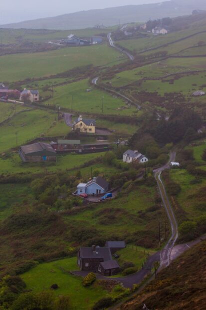 A winding rural road passing through lush Irish countryside with scattered houses and green fields