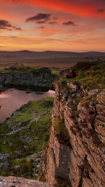 A person sitting on a cliff in the Irish countryside during a colorful sunset
