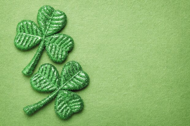 Two green shamrock glitter decorations on a green textured surface