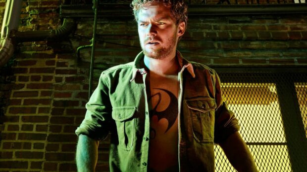 A man with an Iron Fist tattoo on his chest standing in front of a brick wall