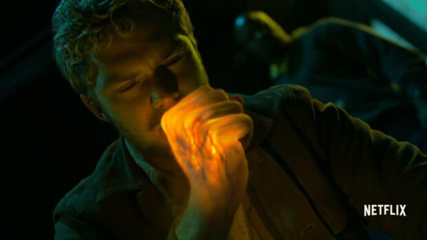 A man with iron fist glowing power clenches his fist in a dark room