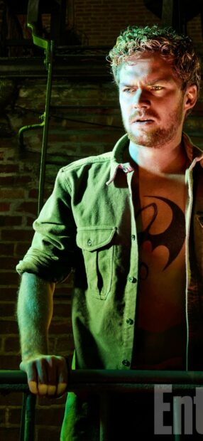 A man with an Iron Fist tattoo stands gripping a railing in a green shirt