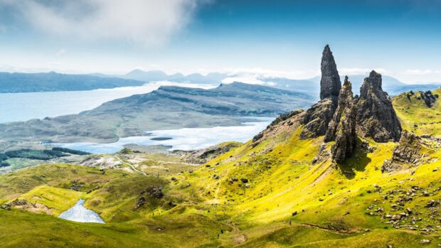 Landscape of Isle Of Skye with tall rock formations and green hills under clear blue sky