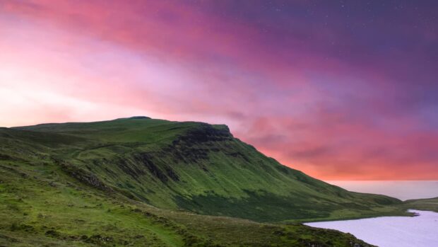 Rolling green hills of Isle of Skye landscape under a vibrant colorful sunset sky