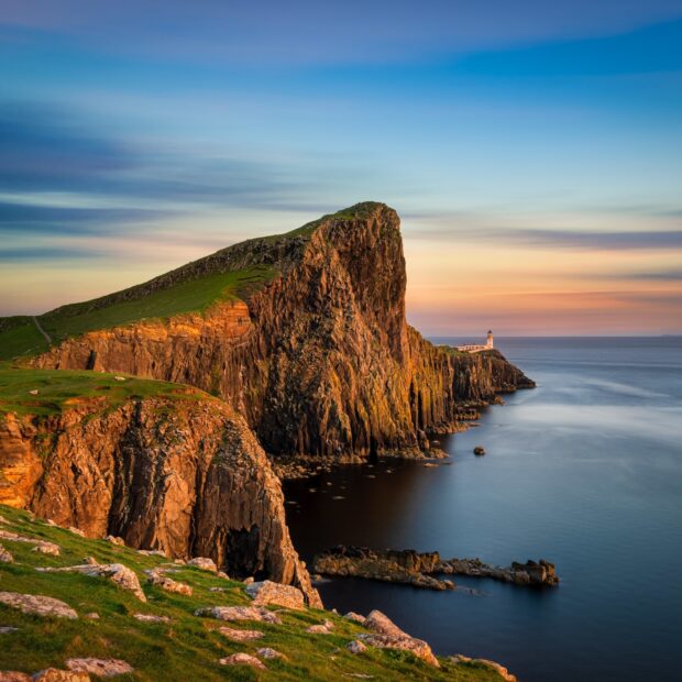 Sunset over rugged Isle of Skye coastline with grassy cliffs and a distant lighthouse