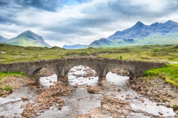 Ancient stone bridge over a rocky river in the Isle of Skye surrounded by lush green hills