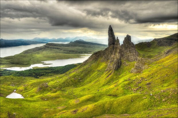 The Isle of Skye landscape features rocky formations and lush green hills under a cloudy sky