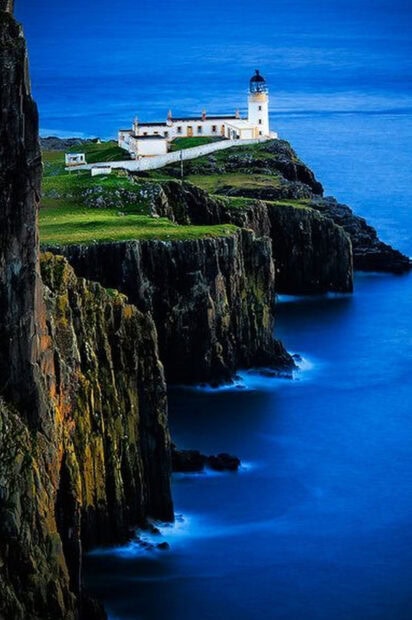 Lighthouse on Isle of Skye cliff with blue sea under twilight sky