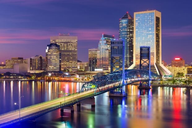 A beautiful skyline of Jacksonville with a lit up steel bridge over the river at dusk