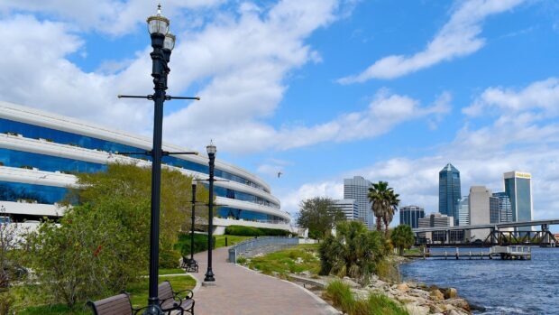 A scenic view of Jacksonville city skyline along the river with a walkway and street lamps