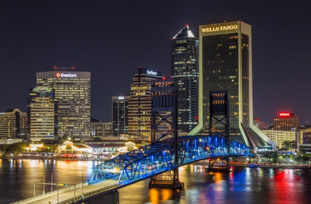 Night view of Jacksonville city skyline with blue lit bridge over the river