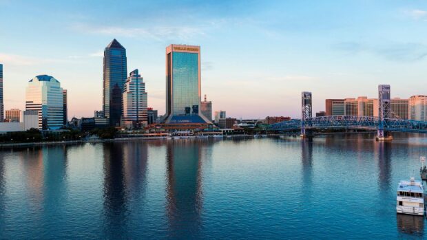 The Jacksonville city skyline reflecting on the river during sunset with iconic buildings and a bridge