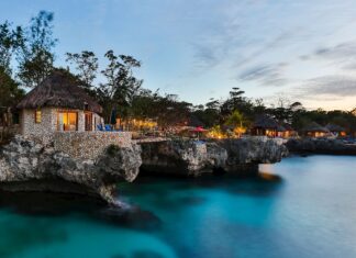 Cozy stone cottages on Jamaica cliffs overlooking calm turquoise water at sunset