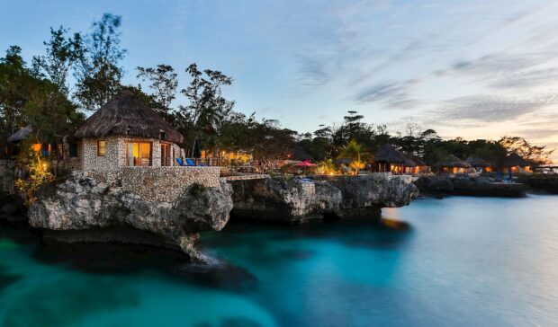 Cozy stone cottages on Jamaica cliffs overlooking calm turquoise water at sunset