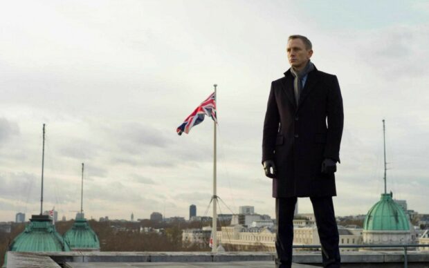 James Bond character standing on rooftop with Union Jack flag and cityscape in the background