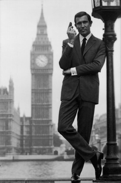 James Bond holding a gun and leaning on a lamppost in front of Big Ben in London