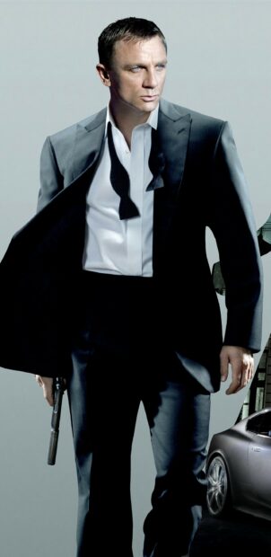 James Bond dressed in a tuxedo holding a gun standing next to a sports car