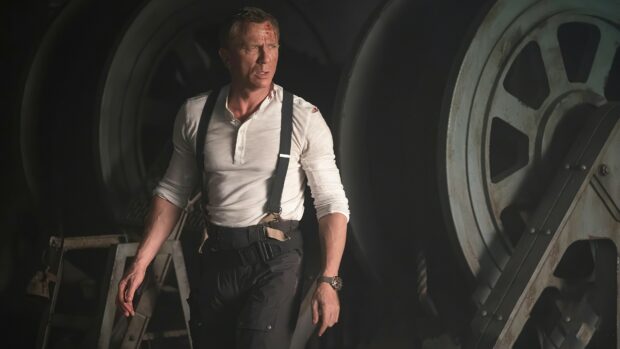 James Bond character in a white shirt and suspenders standing in an industrial setting with large machinery in the background
