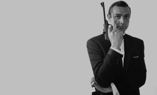 James Bond holding a gun in a classic pose wearing a tuxedo in black and white photo