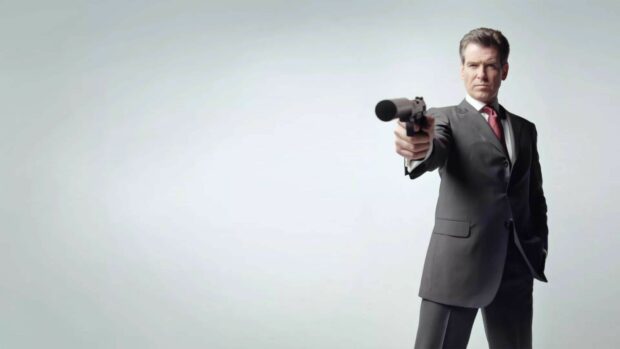James Bond is holding a silenced gun wearing a suit against a plain background