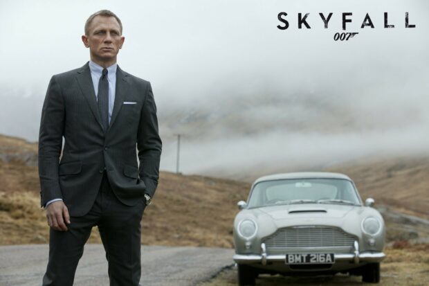 James Bond standing in a suit next to a vintage car in a misty landscape from Skyfall