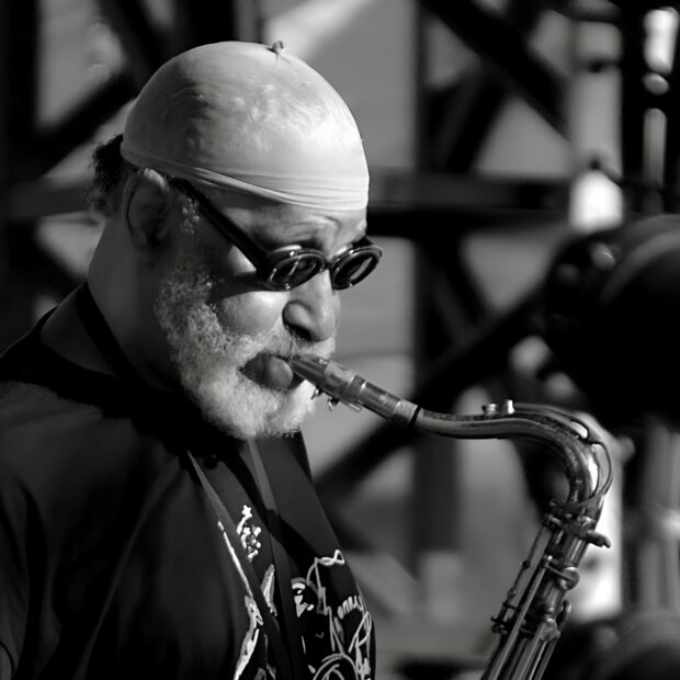 An elderly jazz musician playing saxophone with passion wearing glasses and a cap