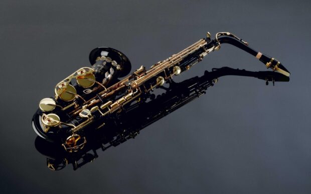A close up of a saxophone reflecting on a black surface with jazz details