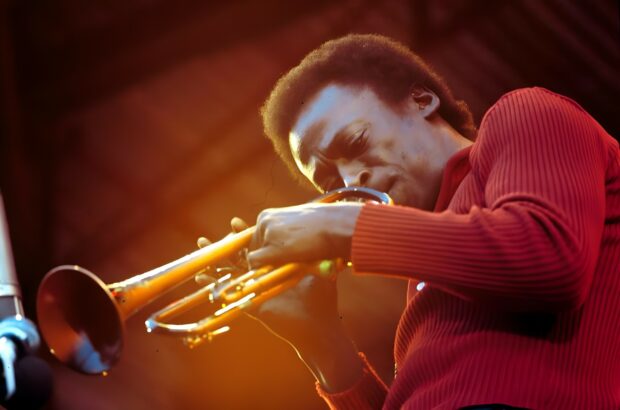 A jazz musician playing the trumpet passionately on stage in a cozy red sweater