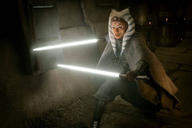 A Jedi warrior with white facial markings wielding two glowing lightsabers in a dark setting