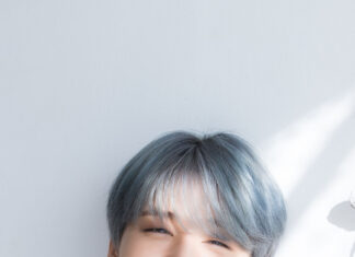 Smiling Jimin wearing red sweater and silver earrings in bright natural light