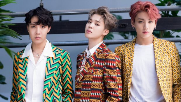 Jimin standing confidently in vibrant patterned suits among band members in a photoshoot setting